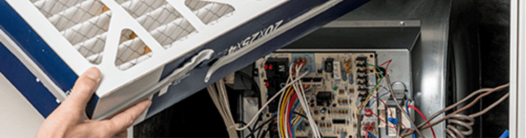 A technician inserts a new furnace filter into a furnace during routine maintenance.
