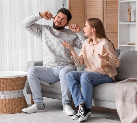 A couple sits in their living room visibly frustrated with their noisy HVAC system.