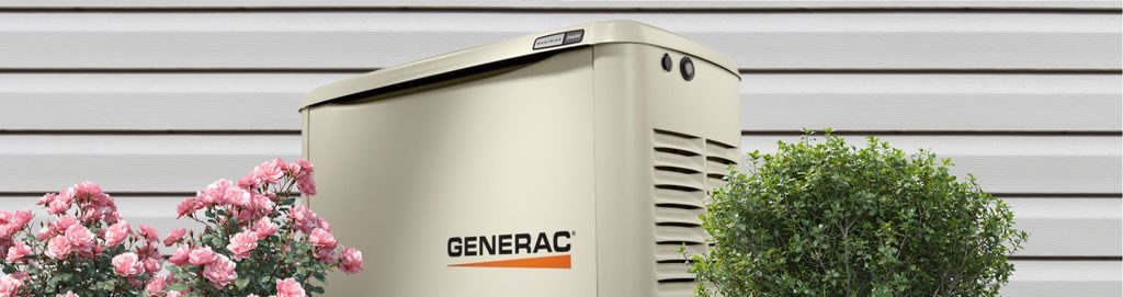 Generac generator beside a house with flowers, and a bush.

